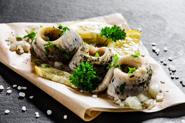 Marinated herring fillets on piece of paper on black stone