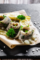 Marinated herring fillets on piece of paper on black stone