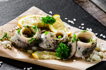 Marinated herring fillets on piece of paper on black stone