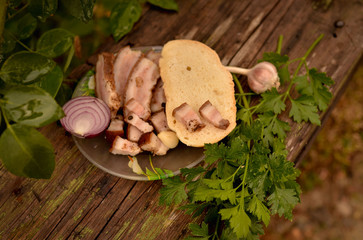 Homemade salted bacon with cold cuts on a baguette. Spicy fat with garlic, onions and parsley. Lunch in the village. Photo in warm colors, on the street. Table made of natural aged wood.