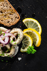 Marinated herring fillets with slices of bread on black stone