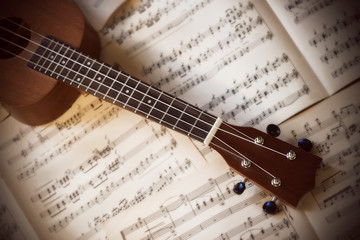 Fototapeta na wymiar A small four-stringed ukulele with nylon strings lies on old white scattered pages of sheet music.