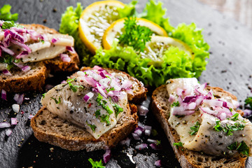 Marinated herring fillets on slices of bread on black stone