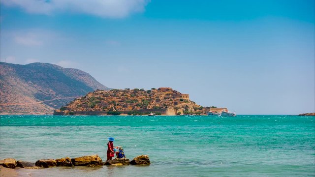 View of Spinalonga island on a Sunny summer day with pleasure boats and holidaymakers in the foreground.