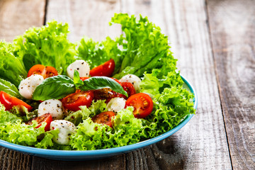 Salad with mozzarella cheese and cherry tomatoes on wooden table
