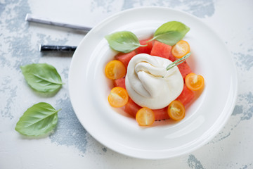 White plate with burrata, watermelon and tomatoes salad, studio shot on a white concrete background