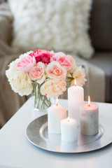 decoration, hygge and cosiness concept - candles burning on table and flowers at cozy home