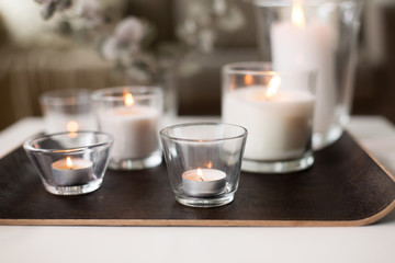 decoration, hygge and cosiness concept - burning white fragrance candles on tray table at cozy home