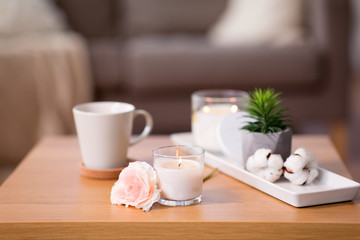 decoration, hygge and cosiness concept - burning fragrance candle and flower bunch on wooden table