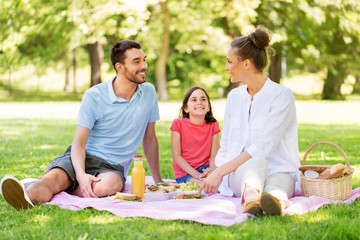 family, leisure and people concept - happy mother, father and daughter having picnic at summer park