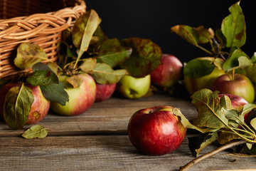 wooden surface with apples and leaves near wicker basket isolated on black