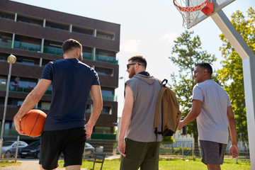 sport, leisure games and male friendship concept - group of men or friends going to play basketball outdoors
