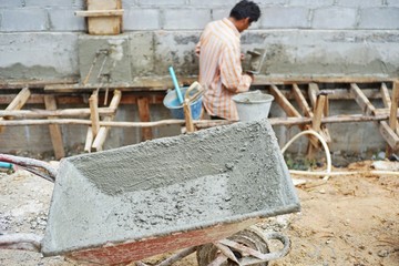 Selective focus on mixed cement cart at construction site with blurred worker in background