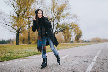 Young beautiful smiling girl in casual wear roller skating listens to music. Autumn walk in the fresh air.