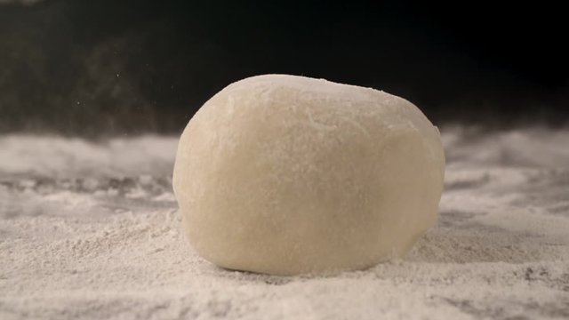 Yeast dough with flour on the kitchen table, cooking food in dark key, cooking in slow motion side view