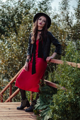 Bright portrait of brunette woman in a red dress and black jacket posing on nature. Fashion beauty photo