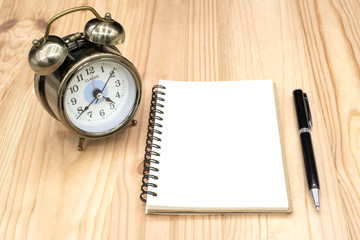 Blank notebook with pen and clock on the table