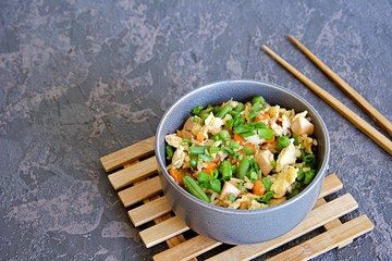 Fried rice with green green beans, carrots, egg and ham in a gray bowl on a dark brown concrete background. Selective focus. Asian food. Copy space.
