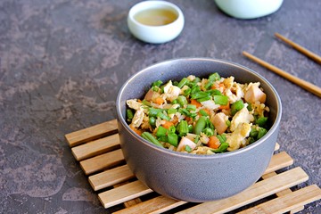 Fried rice with green green beans, carrots, egg and ham in a gray bowl on a dark brown concrete background. Selective focus. Asian food. Copy space.