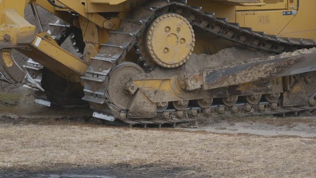 A bulldozer works with soil and sand during construction road works. A bulldozer rides backwards. Tracked track close-up