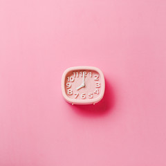 Pink alarm clock lying on yellow and pink surface background. Top view. Square image.
