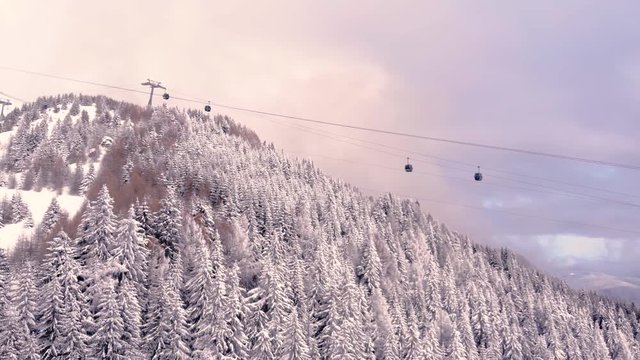 Aerial view over snowy mountain forest valley with clouds, cable car lifting. Outdoor snow alpine wild natural ski resort. Transportation in winter. High altitude gondola in winter. Ski Gondola