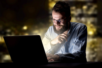 Young handsome businessman working late at night in the office with city lights in the background