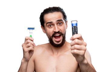Bearded man with mustache chooses between electric razor and old shaving stick standning bare...