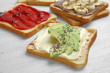 Slices of bread with different toppings on white wooden table
