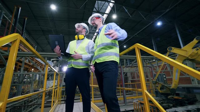 Colleagues stand in a factory facility, checking the work of factory machines.