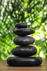 Obraz na płótnie Canvas Table with stack of stones and blurred green leaves on background. Zen concept