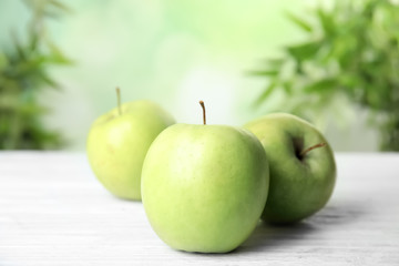 Fresh ripe green apples on white wooden table against blurred background, closeup view. Space for text