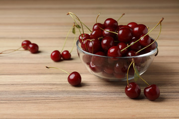 Glass bowl of delicious cherries on wooden table, space for text
