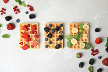 Flat lay composition with delicious waffles and fresh berries on light marble table