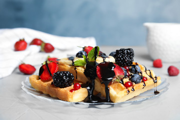 Delicious waffles with fresh berries served on table against blue background