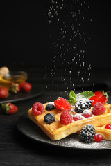 Delicious waffles with fresh berries and powdered sugar served on black wooden table. Space for text