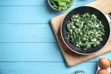 Flat lay composition of tasty cooked spinach and space for text on light blue wooden table. Healthy food