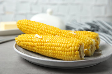 Plate of tasty boiled corn cobs with butter on light grey table