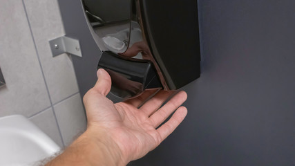 Close up of tan hand pushing soap dispenser under a warm light inside a bathroom.
