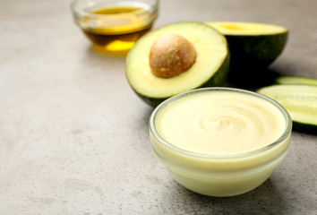Handmade face mask in glass bowl and avocado on grey table