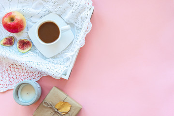 Healthy breakfast on a tray, coffee or cocoa, apple and sliced figs, knitted napkin, candle and gift in a box. Pink background, autumn concept. Top view, flat lay, copy space.