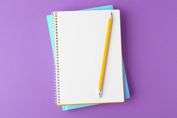 Notebooks with pencil on purple background, top view