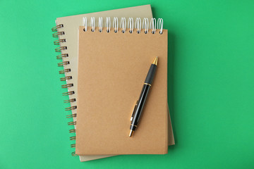 Notebooks and pen on green background, top view