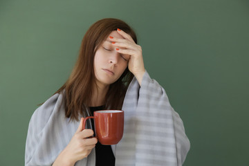 Flu, cold or allergy symptom. Studio shot of young feverish woman wrapped in a blanket and having a cup of tea.