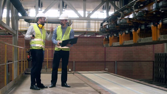Factory workers check a machine that moves bricks.