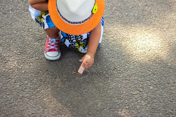 child drawing with chalk on asphalt. boy playing alone in the street. holding a piece of chalk in his fingers