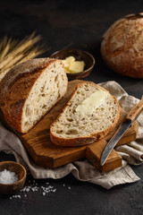 Whole grain bread with flax seeds. Slices of bread with butter on a wooden board. Dark background