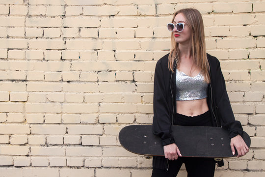 fashion woman with a skateboard on brickwall background. Girl in sunglasses posing with longboard
