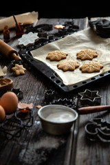 Obraz na płótnie Canvas baked christmas gingerbread cookies on baking tray with parchment on rustic wooden table with rolling pin, flour and cookie cutters