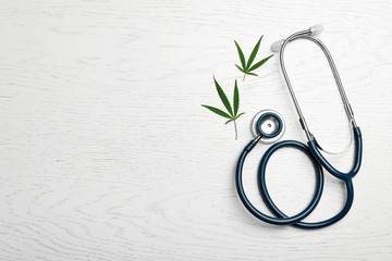 Hemp leaves and stethoscope on white wooden background, flat lay. Space for text